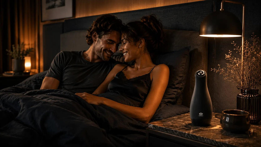 Couple lying in bed together in a dimly lit room with a lamp on a nightstand.